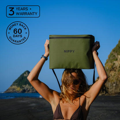 Girl in bikini holding a green NIPPY Cooler bag on her head - at the beach, featuring text about the 3 year warranty and 60 day money-back guarantee.