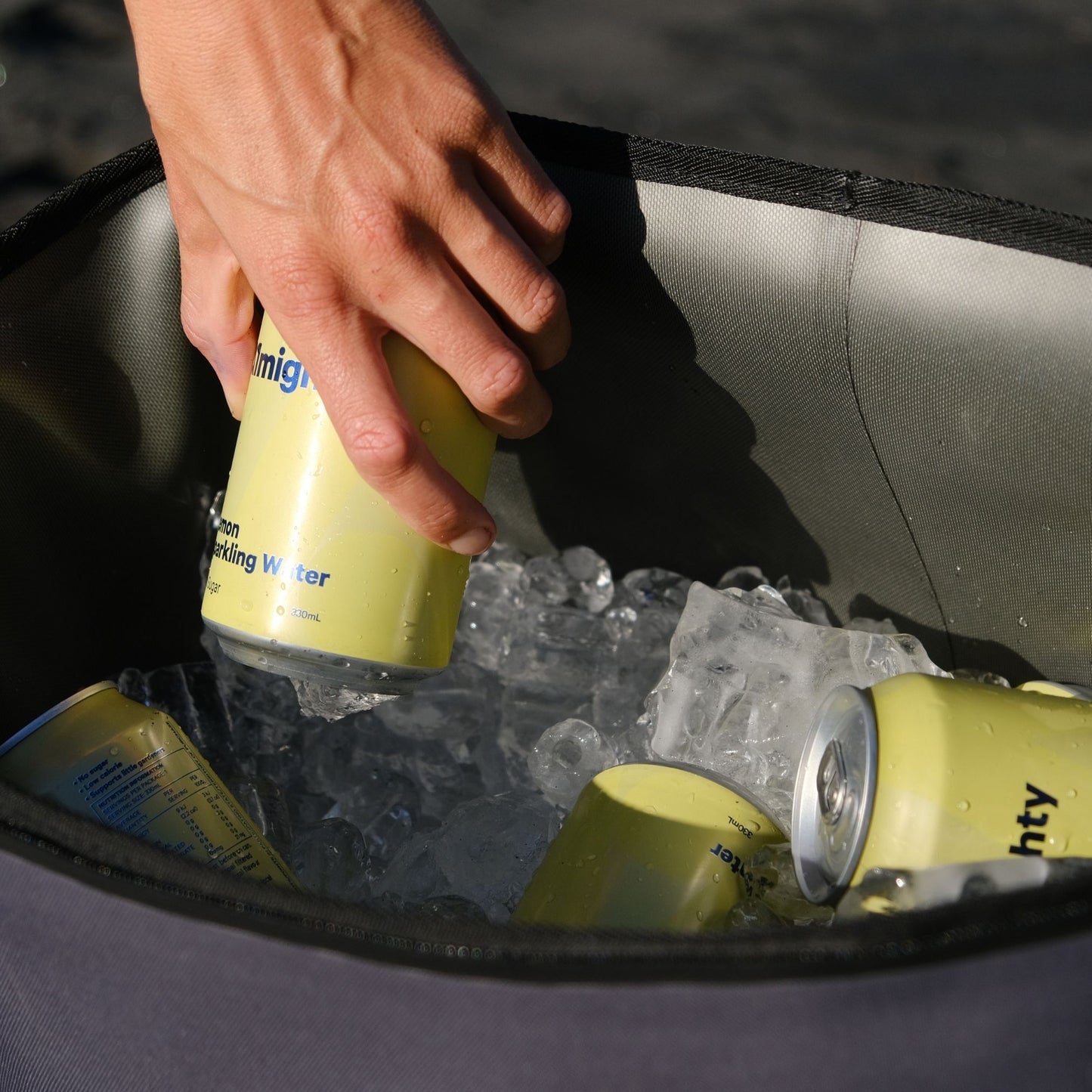 NIPPY 20 liter soft cooler - in colour gray - fill with ice and cold drinks - while a hand reaches in to pull out a cold can of drink
