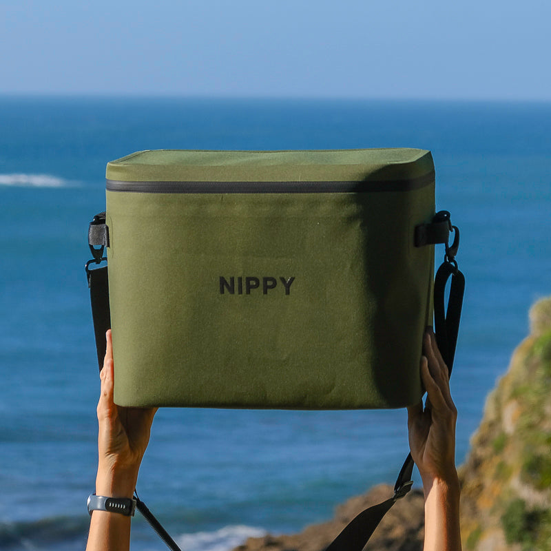 Premium NIPPY Cooler bag being held up in the sky with an ocean view behind it to show the high quality weatherproof materials that stay dry no matter what the weather brings